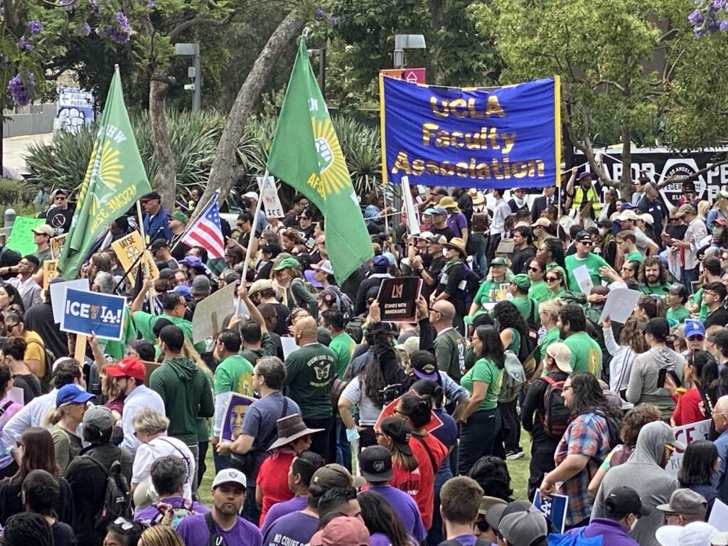A large number of people in a mass rally with union flags. UCLA Faculty Association banner promptly displayed.